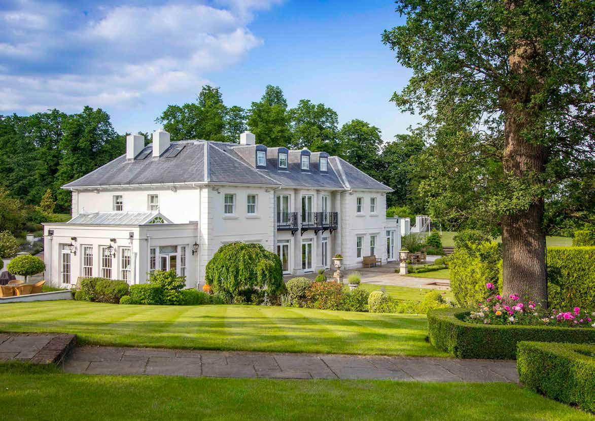 A white rendered country house with a slate roof, photographed across a striped lawn with a mature oak to one side