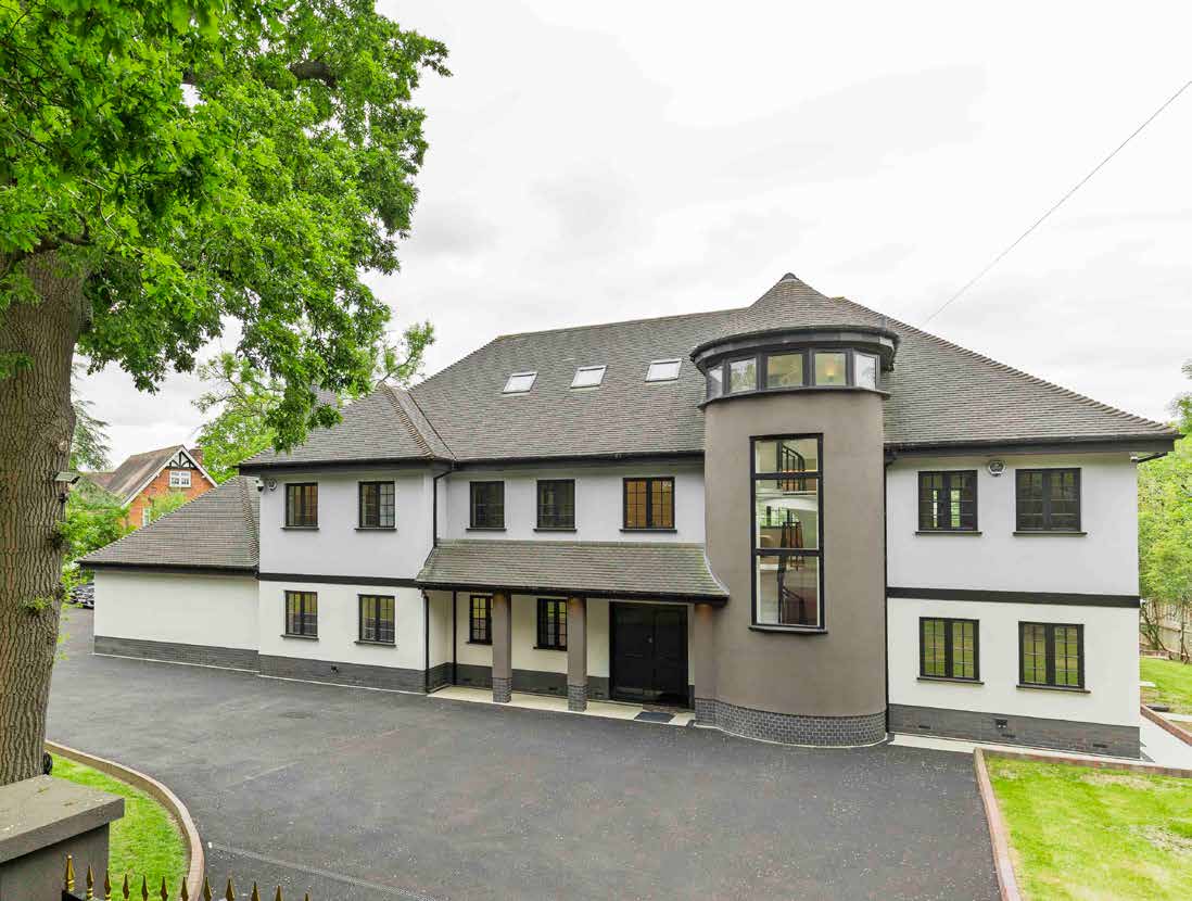 A newly refurbished house with a curved glazed turret and a tarmac drive, photographed on an overcast day