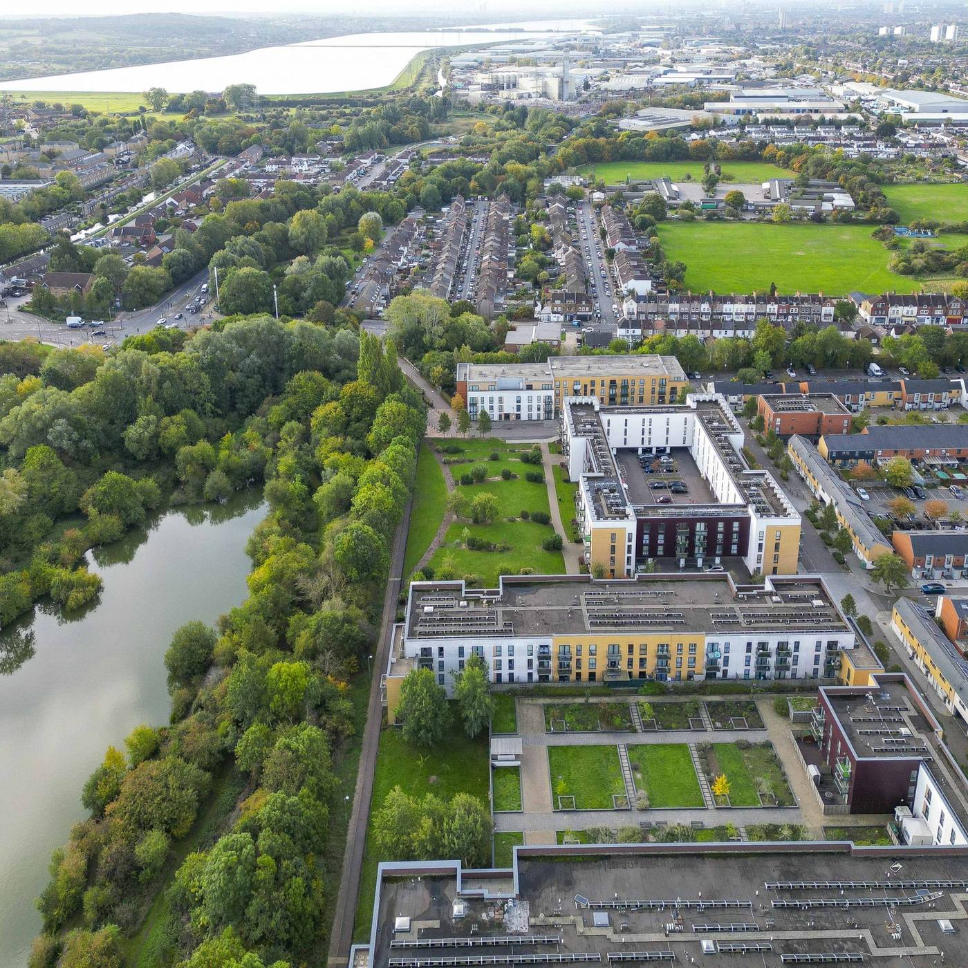 An aerial view of a riverside town, with apartment blocks, terraced streets, playing fields and a lake below