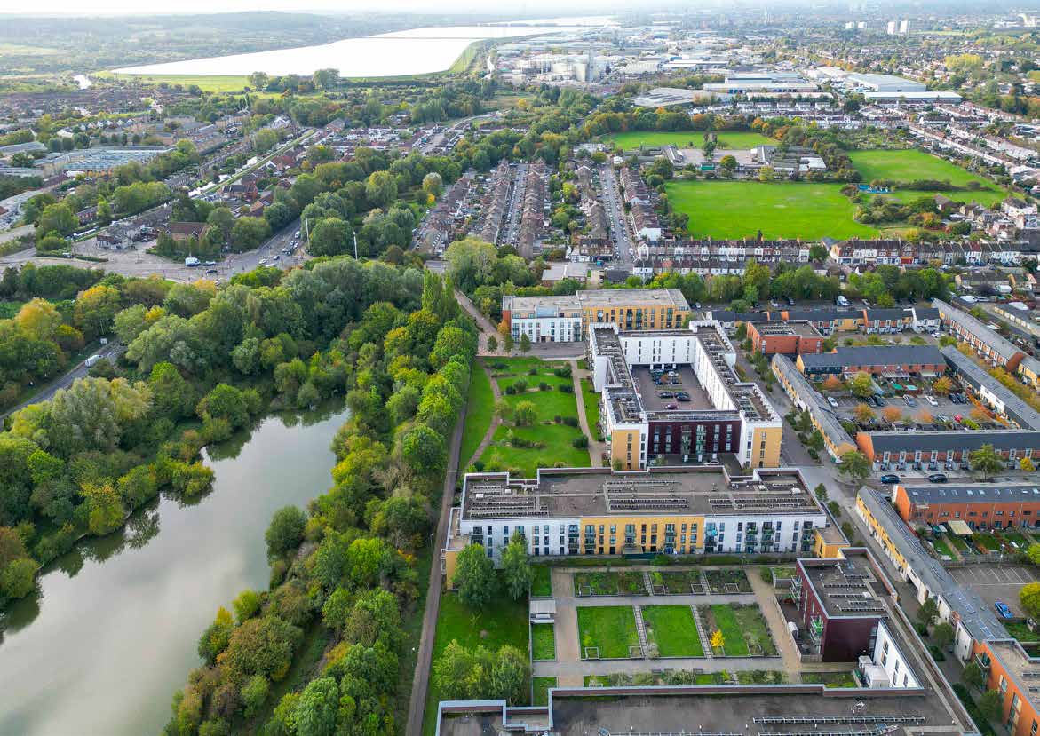 An aerial view of a riverside development, with apartment blocks, roof gardens, terraced streets and a lake