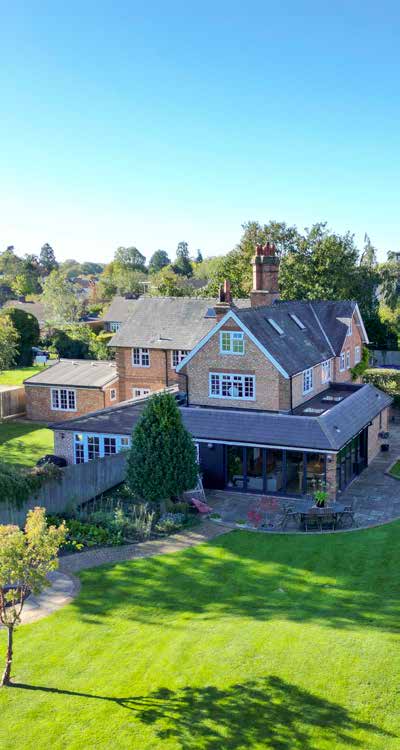 An aerial view of a brick house with a glazed garden room extension, a clipped lawn and a village behind