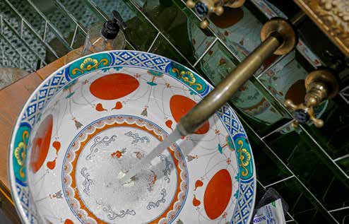 Water running from a brass tap into a hand painted bowl basin against dark green tiles