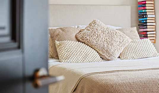 A made bed with textured cream cushions, seen through a part open grey painted door