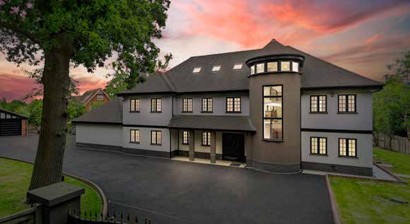 A large rendered house with a curved glazed turret, photographed at dusk under a pink sky with the windows lit