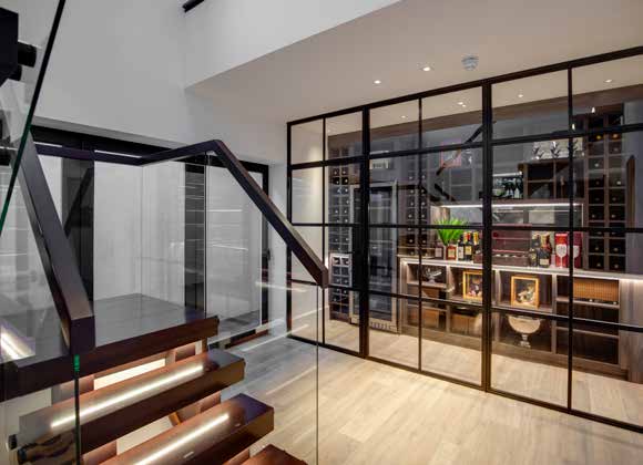 A floating timber staircase with lit treads beside a glazed wine room in a double height hallway