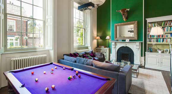 A snooker table with a purple cloth in a green painted drawing room with tall sash windows and a marble fireplace