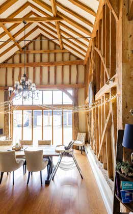 A converted barn dining area with an exposed oak truss roof, a chandelier and full height glazing