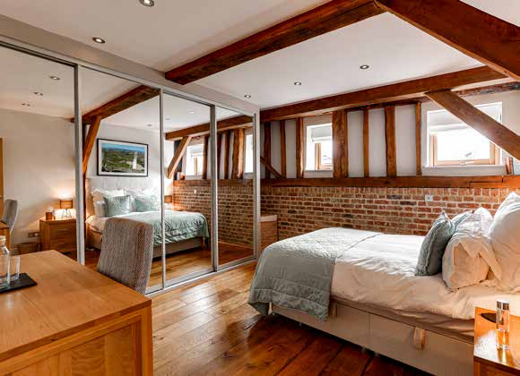 A bedroom under sloping beams with an exposed brick wall, mirrored wardrobes and a wood floor