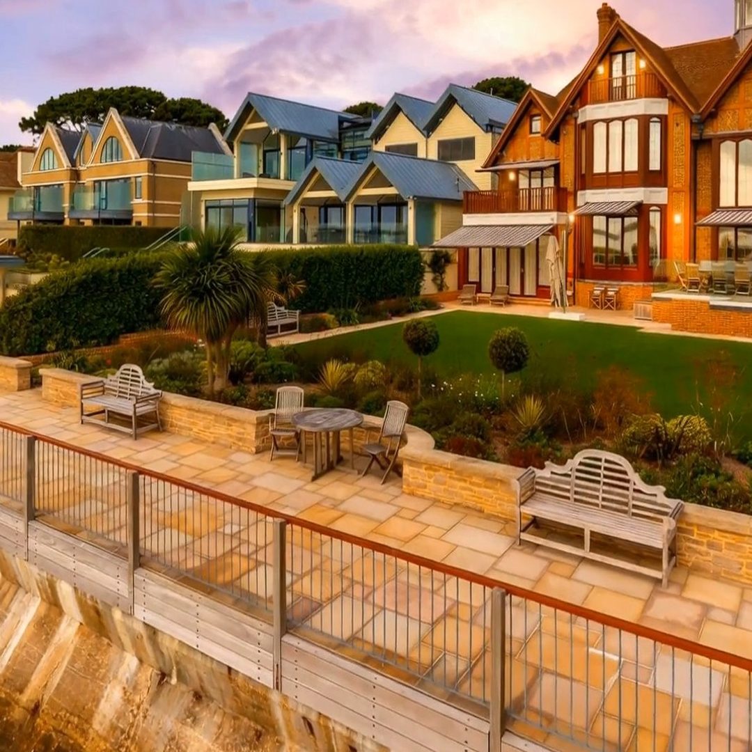 A row of waterfront houses and a terraced garden photographed at sunset with a pink and lilac sky