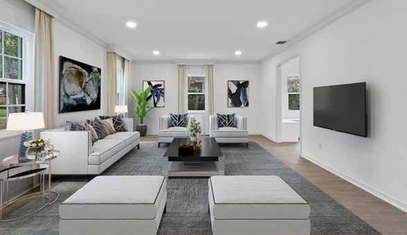 The same room staged as a living room with a sofa, two armchairs, ottomans, a rug, artwork on the walls and a wall mounted television
